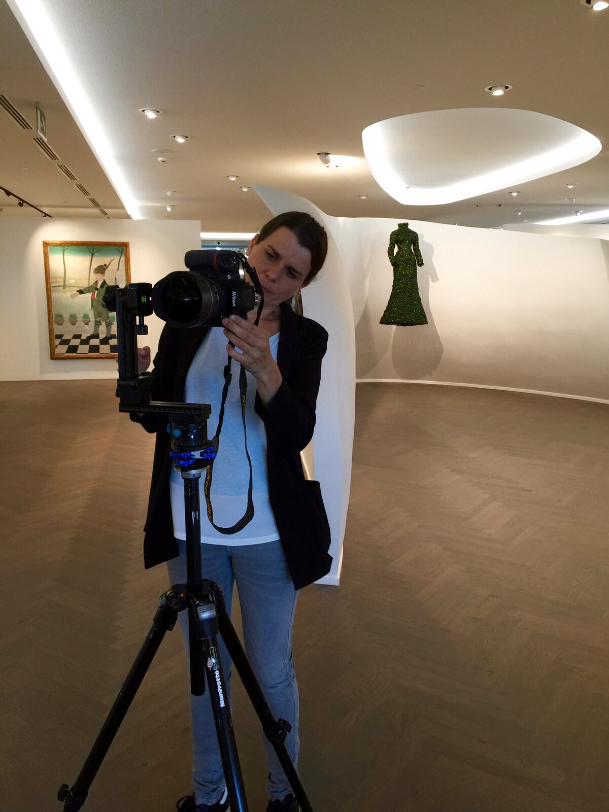 Photographer adjusting a Nikon DSLR mounted on a panoramic tripod head in a bright gallery.