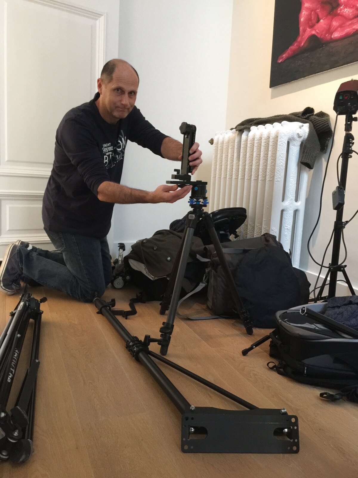 Crew member kneeling beside a panoramic camera rig, tripod, lighting stands and equipment bags.